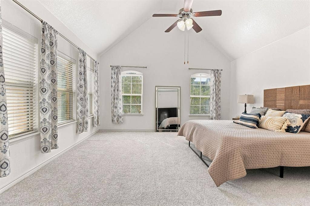 5605 Cojimar Drive, McKinney, TX 75070 Vaulted ceiling, ceiling fan with integrated lighting, multiple windows with blinds, light-toned carpeting, and a wood-panel accent wall