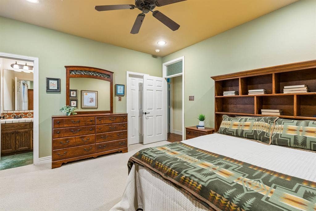 3227 Berry Hollow, Melissa, TX 75454 Guest bedroom #1 located downstairs with ensuite bathroom and large walk-in closet. Ceiling fan with integrated lighting, wood-finish built-in shelving, soft carpet flooring, and a doorway to an adjoining room