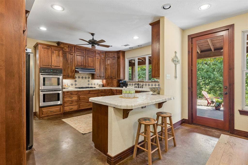 3227 Berry Hollow, Melissa, TX 75454 Warm wood cabinetry, stainless steel double oven, tile backsplash, and a breakfast bar with stone-look countertop