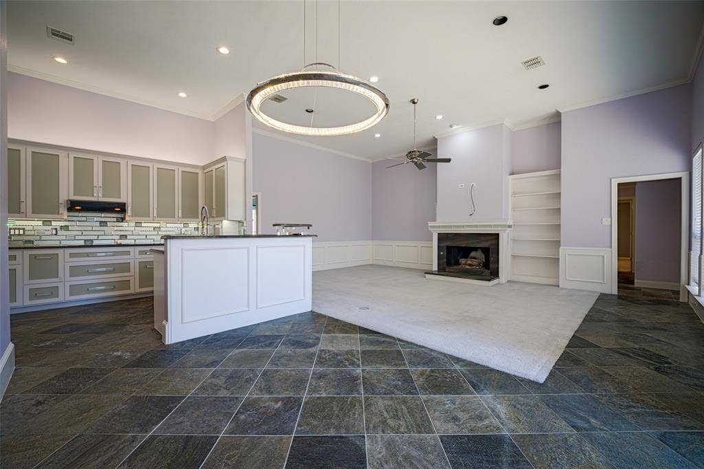 Spacious room featuring a fireplace with a dark surround, built-in shelving, and a ceiling fan