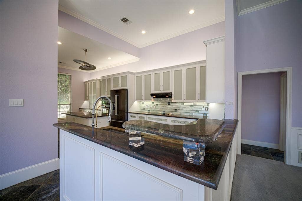 Kitchen featuring a peninsula with a dark countertop, white paneled cabinetry, stainless steel faucet, and a subway tile backsplash
