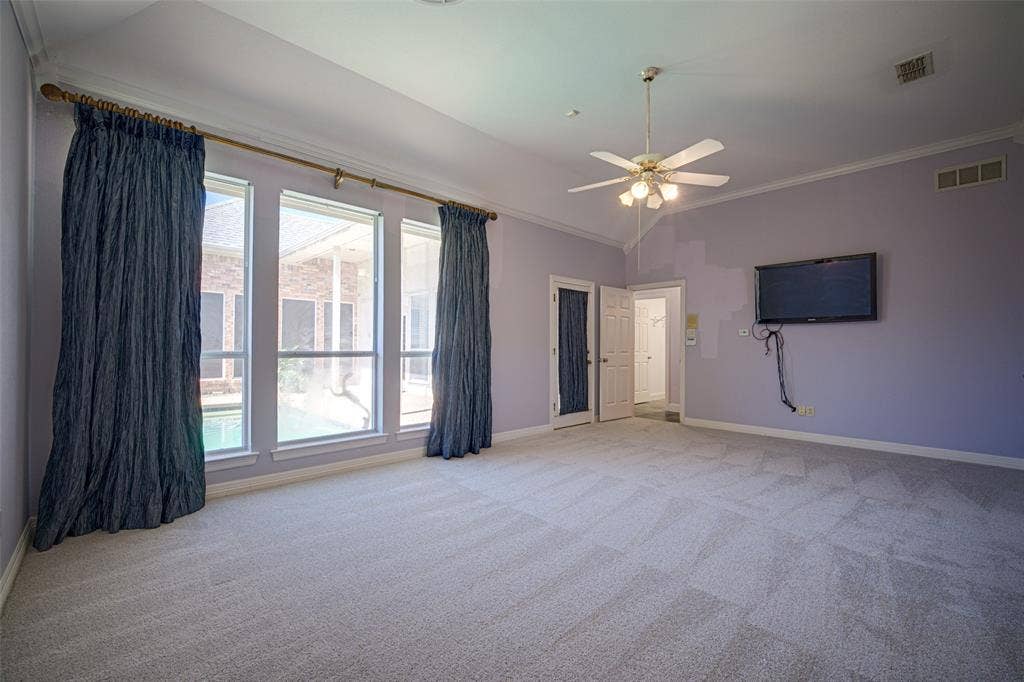 Primary bedroom Vaulted ceiling with crown molding, ceiling fan with light fixture, light gray carpet, and multiple windows