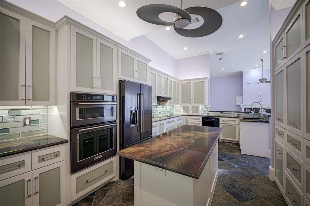 Kitchen featuring an expansive island with a polished countertop, integrated double ovens, and a side-by-side refrigerator