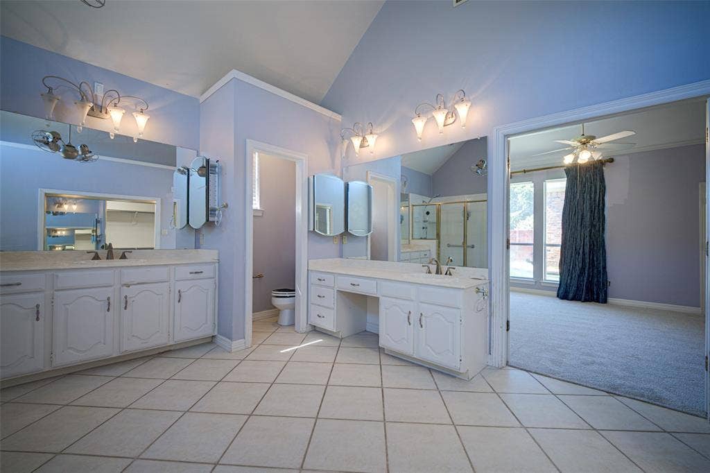 Dual vanity sinks, tile flooring, vaulted ceiling, and ample counter space with built-in storage