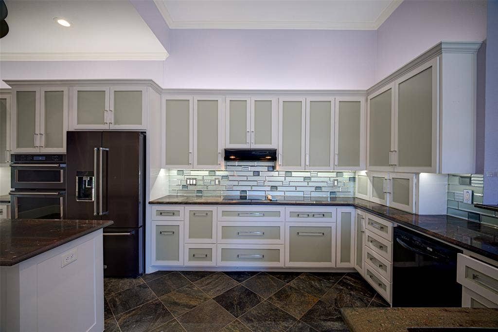 Kitchen with frosted glass-front upper cabinetry, dark stone countertops, mosaic tile backsplash, and built-in stainless steel appliances