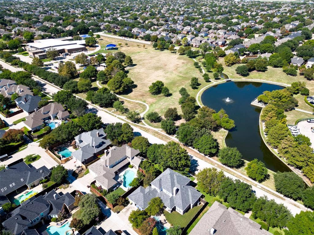 Aerial perspective showcasing a residential community with mature landscaping, a central park, a pond with a fountain, and numerous properties featuring private swimming pools