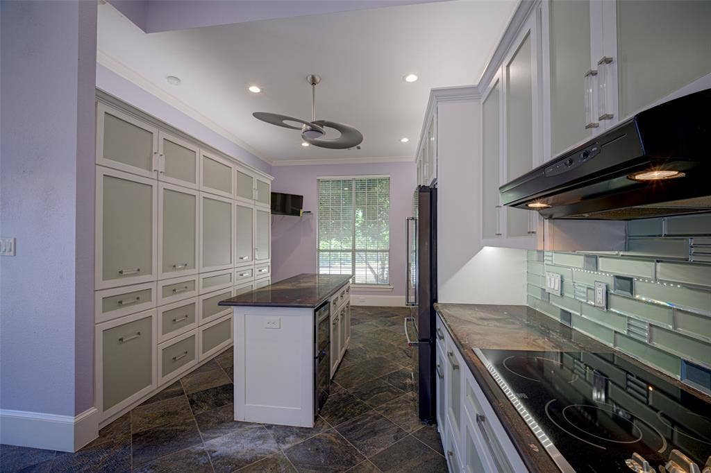Gourmet kitchen featuring a built-in electric cooktop, dark stone countertops, a mosaic tile backsplash, and extensive custom cabinetry