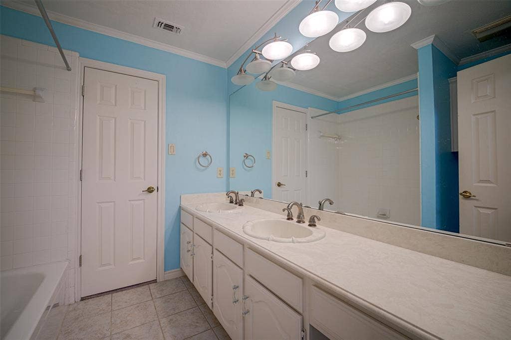 Double vanity with integrated sinks, full-width mirror, overhead vanity lighting, white paneled cabinetry, and tiled flooring