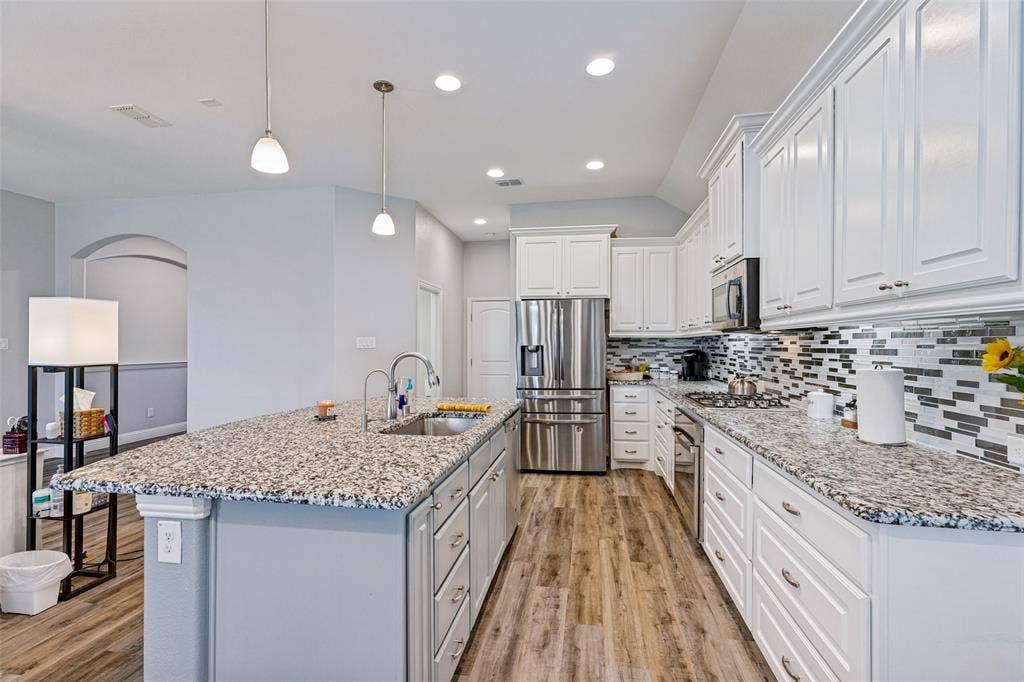 1004 Baynes Drive, McKinney, TX 75071 Kitchen featuring wood-finish flooring, white cabinetry, a large kitchen island with a sink, granite countertops, and stainless steel appliances