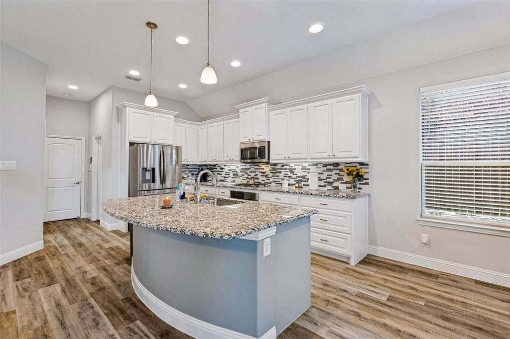 1004 Baynes Drive, McKinney, TX 75071 Kitchen featuring white shaker cabinets, stainless steel appliances, granite countertops, a tiled backsplash, and wood-finish flooring