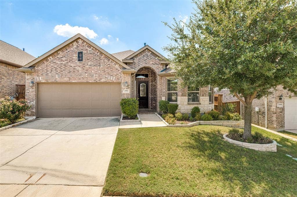 1004 Baynes Drive, McKinney, TX 75071 Brick and stone facade, arched entry, integrated two-car garage, established front yard landscaping, and concrete driveway