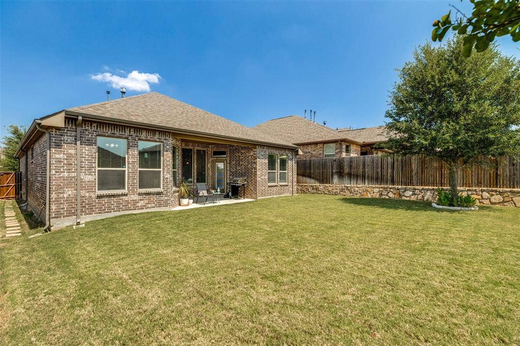 1004 Baynes Drive, McKinney, TX 75071 Expansive backyard featuring a brick exterior, covered patio, and a stone retaining wall