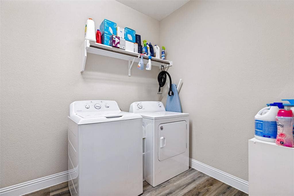 1004 Baynes Drive, McKinney, TX 75071 Laundry area with wood-finish flooring and a wall-mounted shelf. Also room for a small refrigerator.