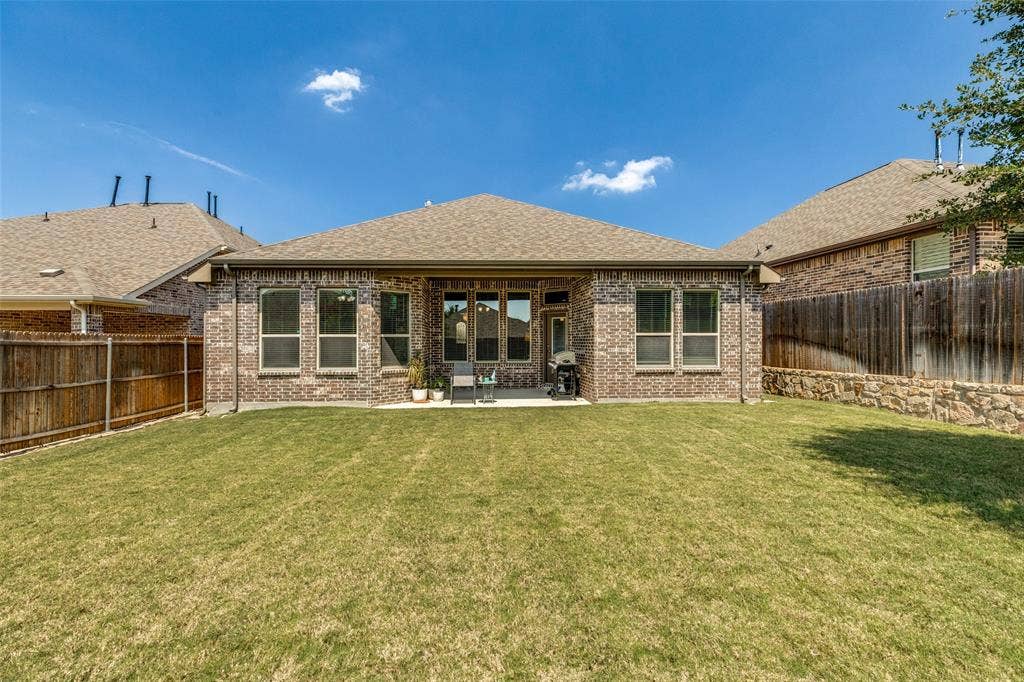 1004 Baynes Drive, McKinney, TX 75071 Expansive backyard featuring a manicured lawn, brick exterior, covered patio, and privacy fencing