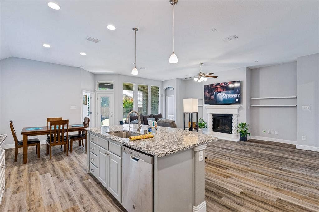 1004 Baynes Drive, McKinney, TX 75071 Open concept living space featuring wood-finish flooring, a kitchen island with stone countertop, recessed lighting, and a fireplace with mantle