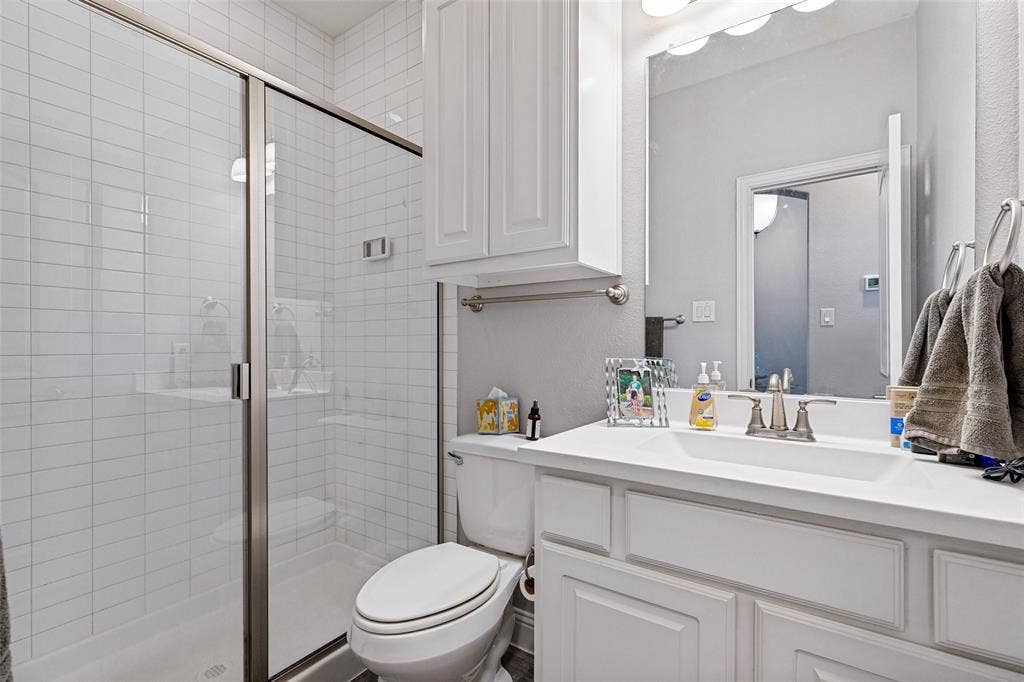 1004 Baynes Drive, McKinney, TX 75071 Glass-enclosed shower with white subway tile, white vanity with integrated sink, brushed nickel faucet, and white wall-mounted cabinetry