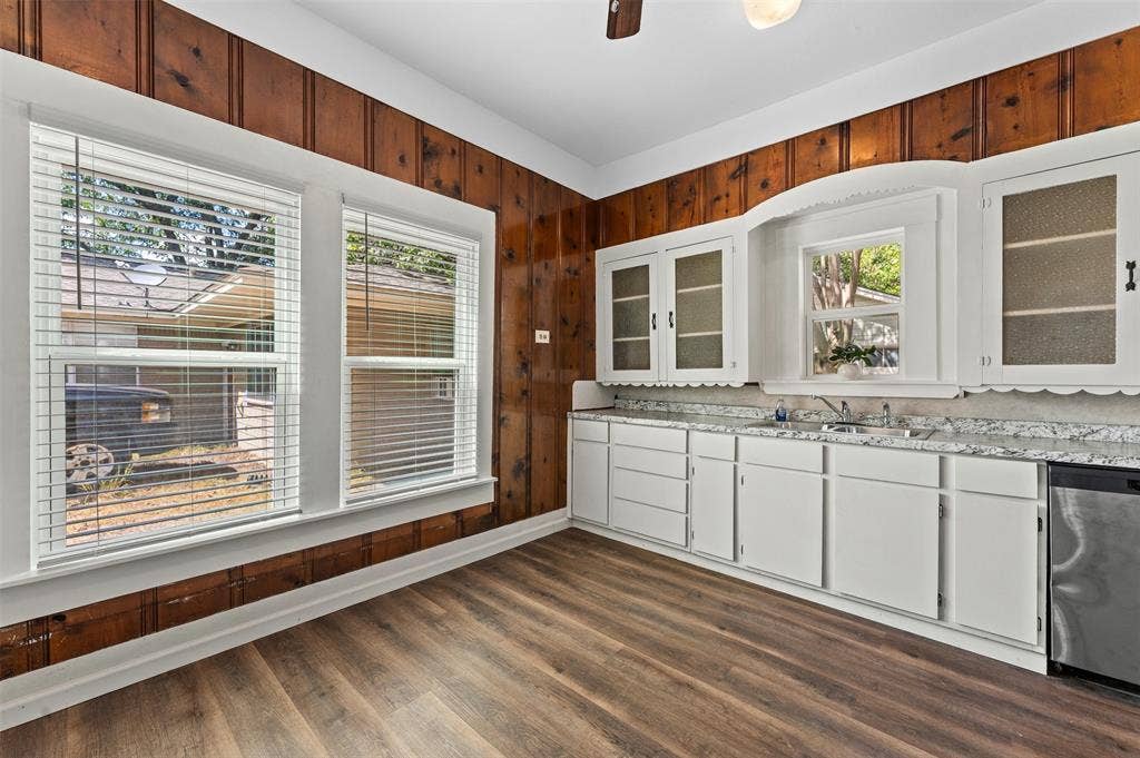 302 W Broadway Street, West, TX 76691 Wood-finish flooring, white cabinetry, textured wood paneling, multiple windows, and a stainless steel dishwasher