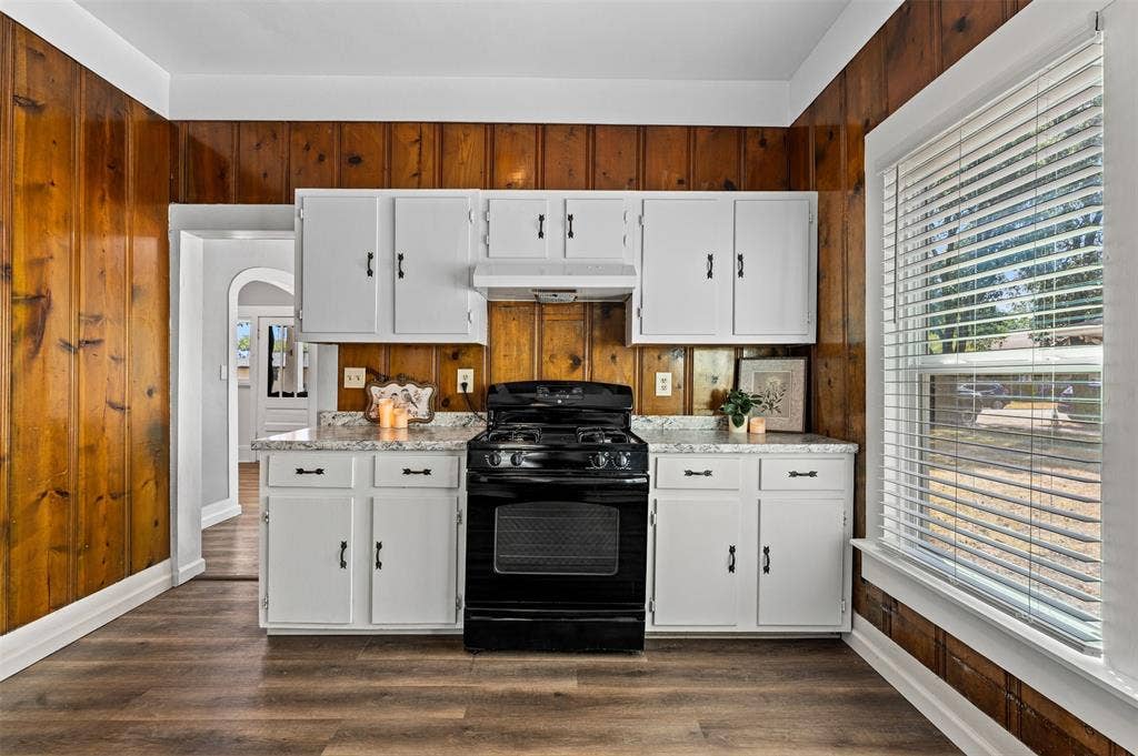 302 W Broadway Street, West, TX 76691 Wood-finish flooring, wood paneling, white cabinetry, a built-in oven range, and a window with blinds
