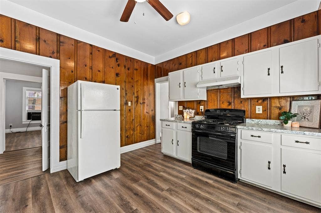 302 W Broadway Street, West, TX 76691 Wood-finish flooring, paneled wood wall, white cabinetry with black hardware, black gas range, and white refrigerator