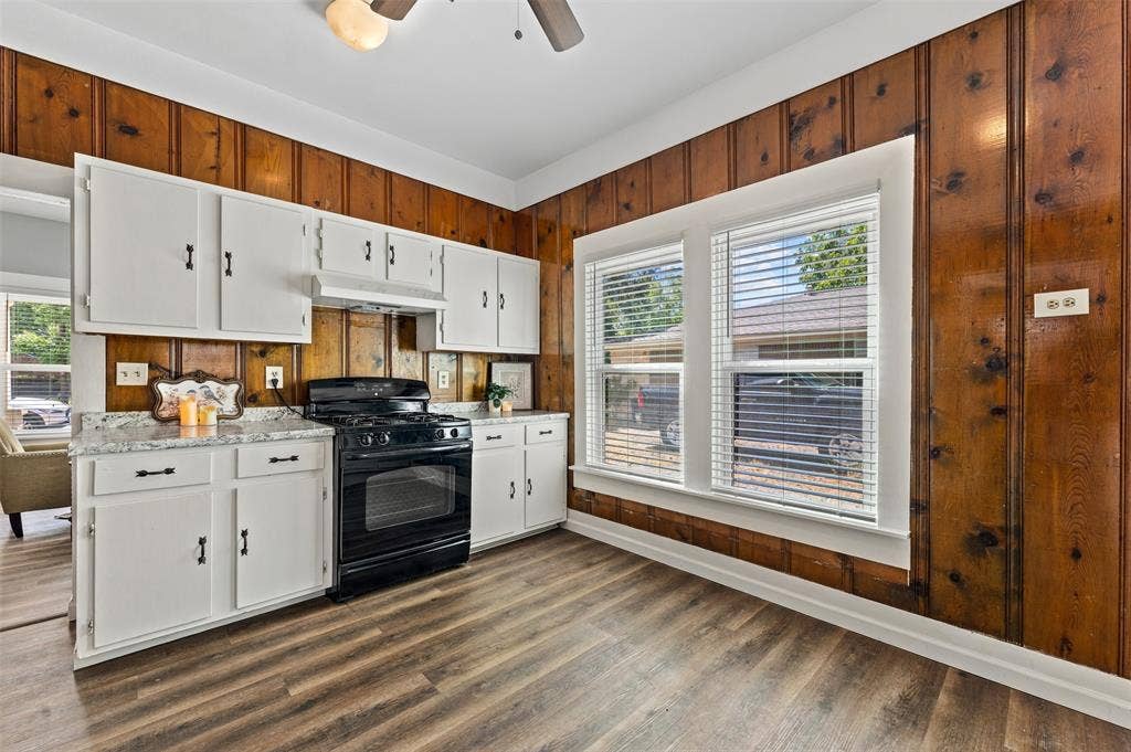 302 W Broadway Street, West, TX 76691 Kitchen featuring wood-finish wall paneling, white cabinetry, light countertops, and wood-finish flooring