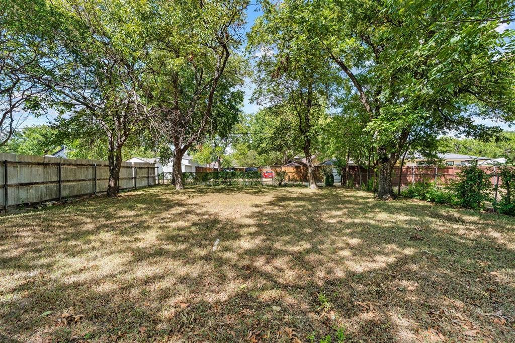 302 W Broadway Street, West, TX 76691 Expansive backyard with a wood privacy fence, mature trees, and natural ground cover