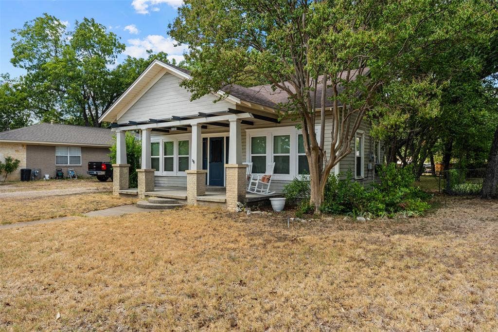 302 W Broadway Street, West, TX 76691 Craftsman-style home featuring a covered front porch with substantial columns, a gabled roofline, and mature trees providing shade