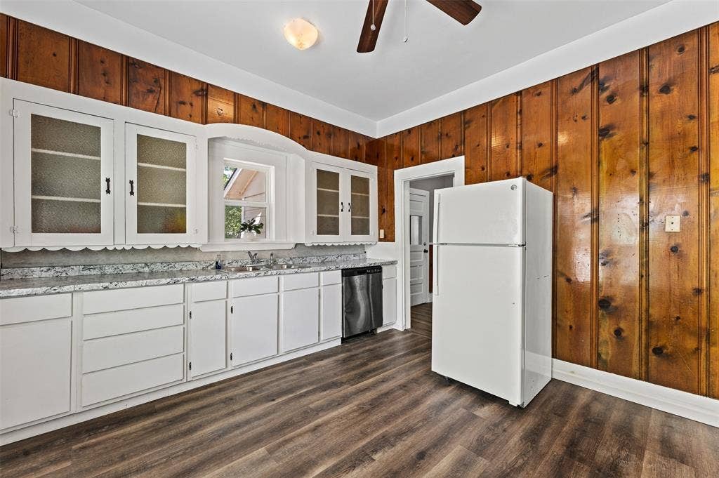 302 W Broadway Street, West, TX 76691 Kitchen featuring wood-finish flooring, white cabinetry with glass-front uppers, light-toned countertops, and wood paneling