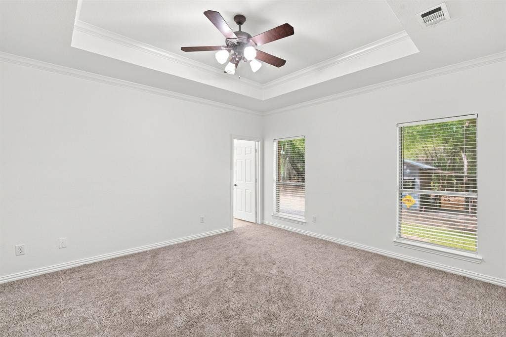 Spacious primary retreat with a tray ceiling, crown molding, and plenty of natural light from dual windows.