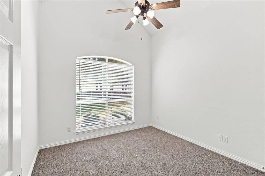 Bright bedroom with a vaulted ceiling, lighted ceiling fan, and an arched window that fills the room with natural light.