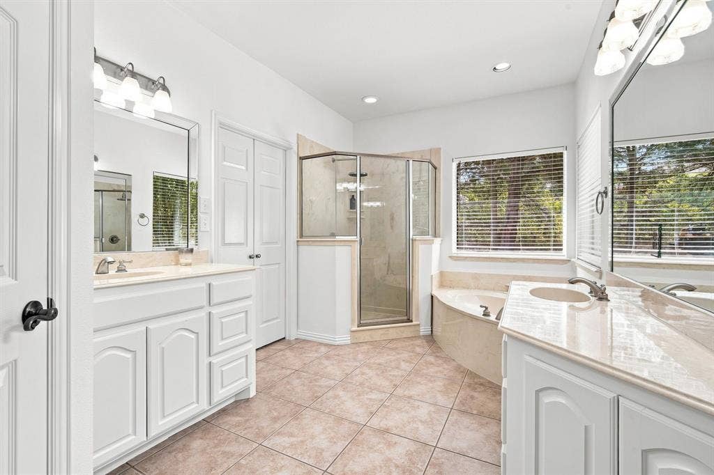 Spa-like primary bath with dual vanities, a glass-enclosed shower, a soaking tub, and elegant tile flooring.