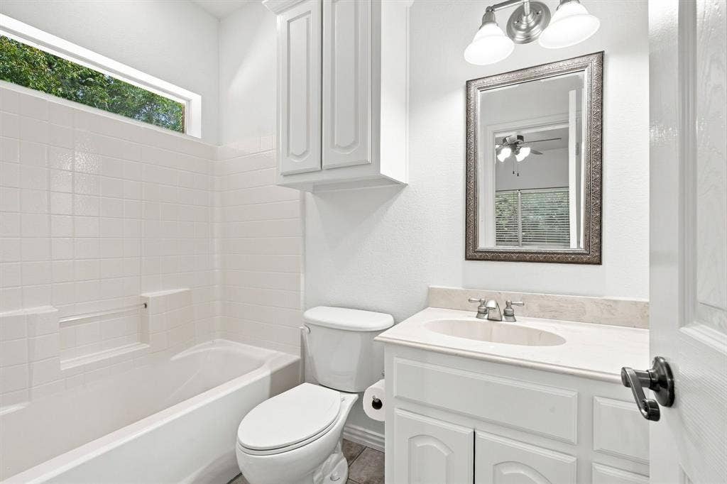 Well-designed bathroom with white ceramic tile surround, a transom window for natural light, and a stone-finish vanity countertop.