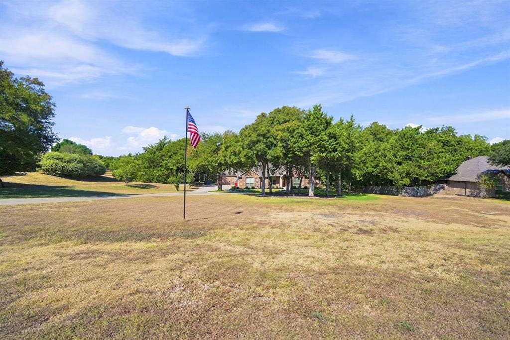 A welcoming driveway winds toward the front of the home, framed by open lawn and mature trees for a picturesque approach.