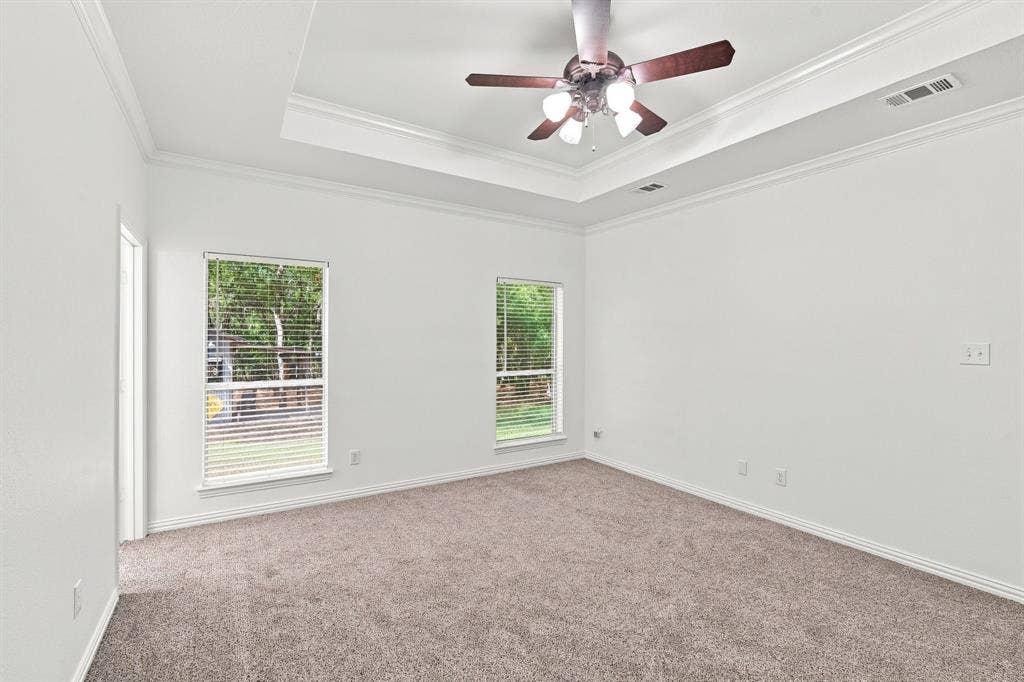 Relaxing primary suite featuring a tray ceiling with crown molding and soft carpeting throughout.