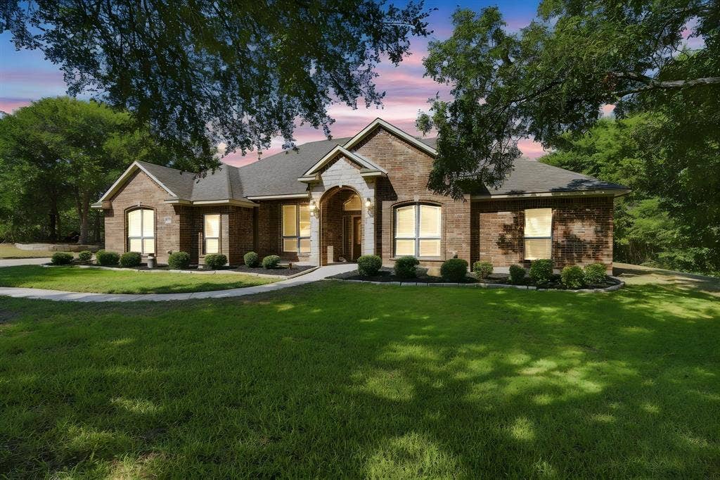 Elegant arched entryway and windows complement the brick and stone exterior, framed by manicured landscaping.
