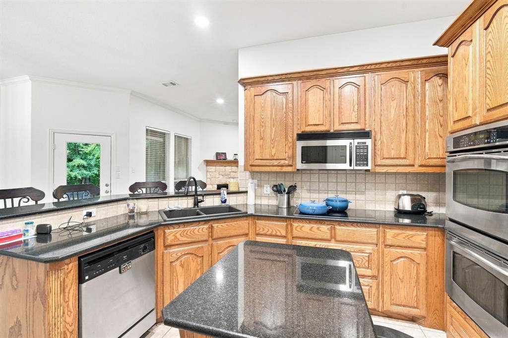 Stylish kitchen with wood cabinetry, sleek granite countertops, a dual-basin sink and tile backsplash.