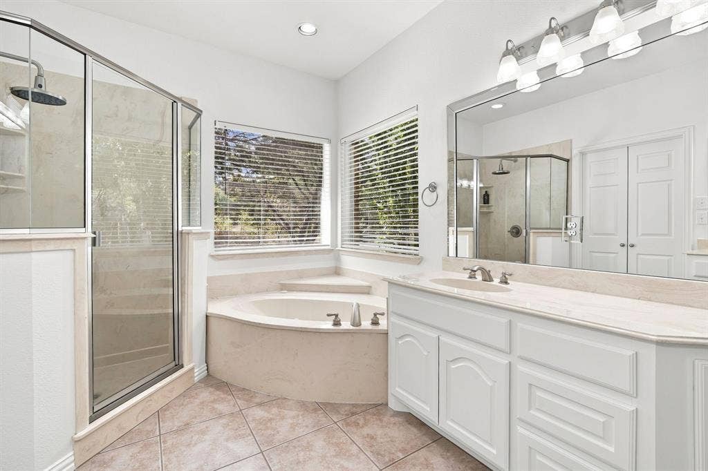 Luxurious primary bath featuring a rainfall shower, corner soaking tub, dual-sink vanity, and an oversized mirror.