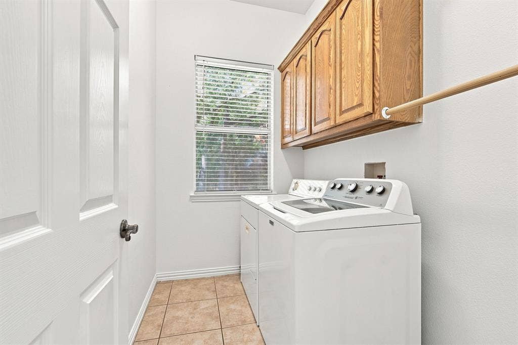 Convenient laundry room with tile flooring, wood-finish cabinetry, and a window for natural light.