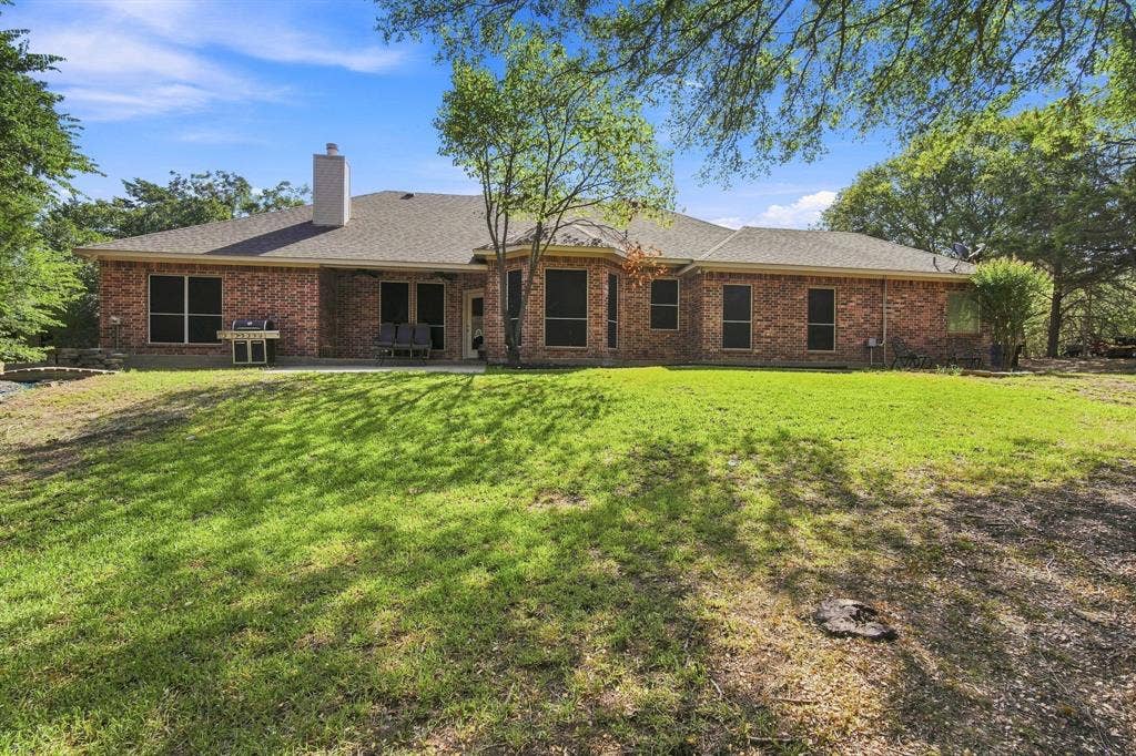 Unwind on the covered patio surrounded by mature trees and a picturesque stone chimney, a true backyard oasis made for morning coffee or evening gatherings.