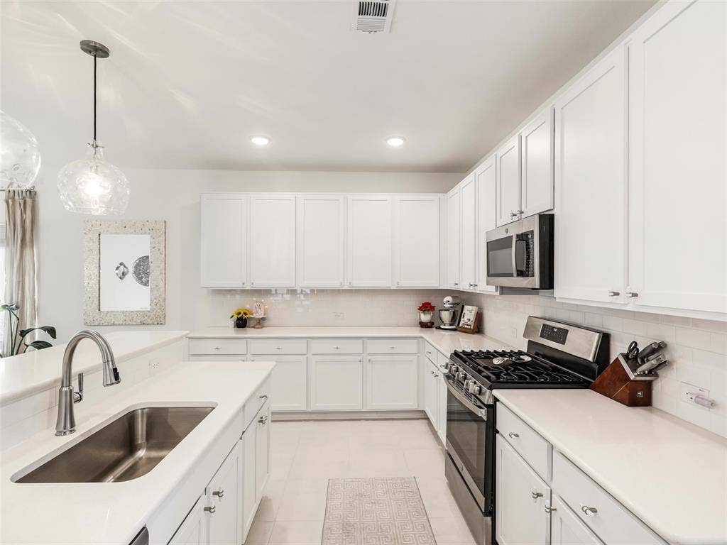 Well-appointed kitchen featuring abundant white cabinetry, stainless steel appliances, a gas range, and a large single-basin sink
