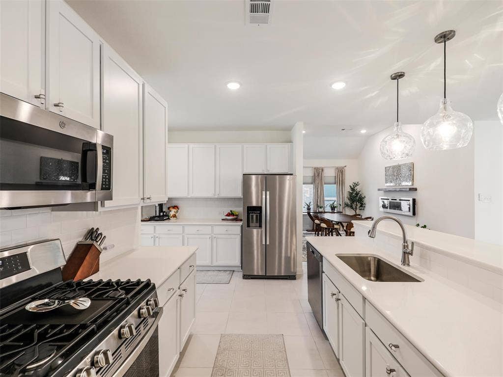 Kitchen featuring extensive white cabinetry, stainless steel appliances, light countertops, and a subway tile backsplash