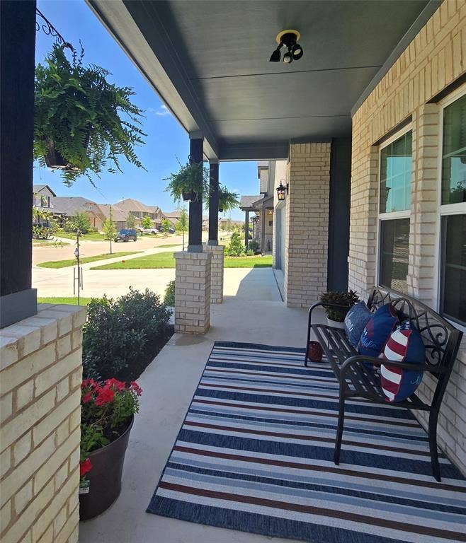 Covered front porch featuring brick columns, recessed lighting, and a concrete surface