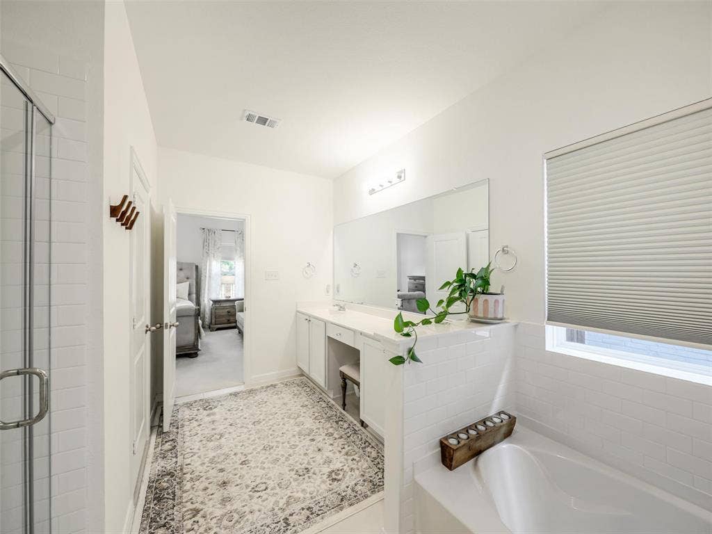 White subway tile shower with glass enclosure, dual vanity with undermount sinks, white countertop, and built-in soaking tub