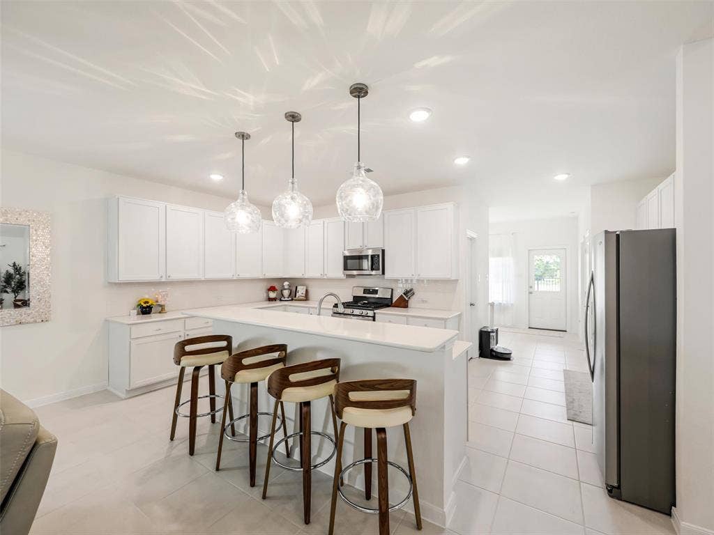 White cabinetry, stainless steel appliances, solid surface countertops, tile flooring, and pendant lighting