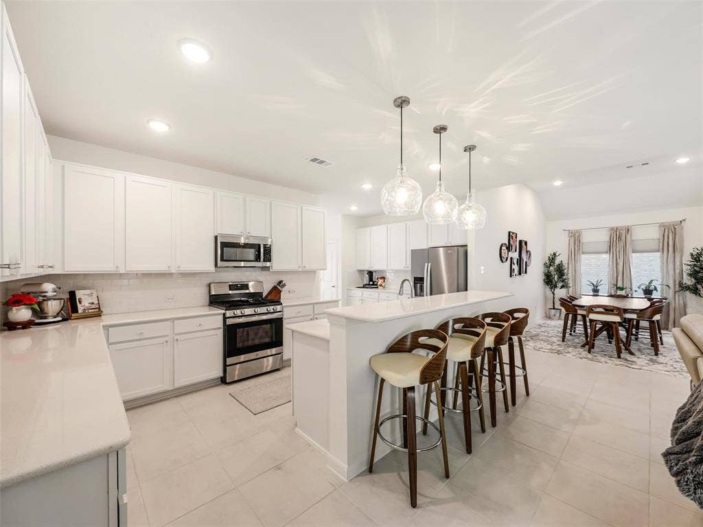 White flat-panel cabinetry, stainless steel appliances, light-toned countertops, tile flooring, and recessed lighting