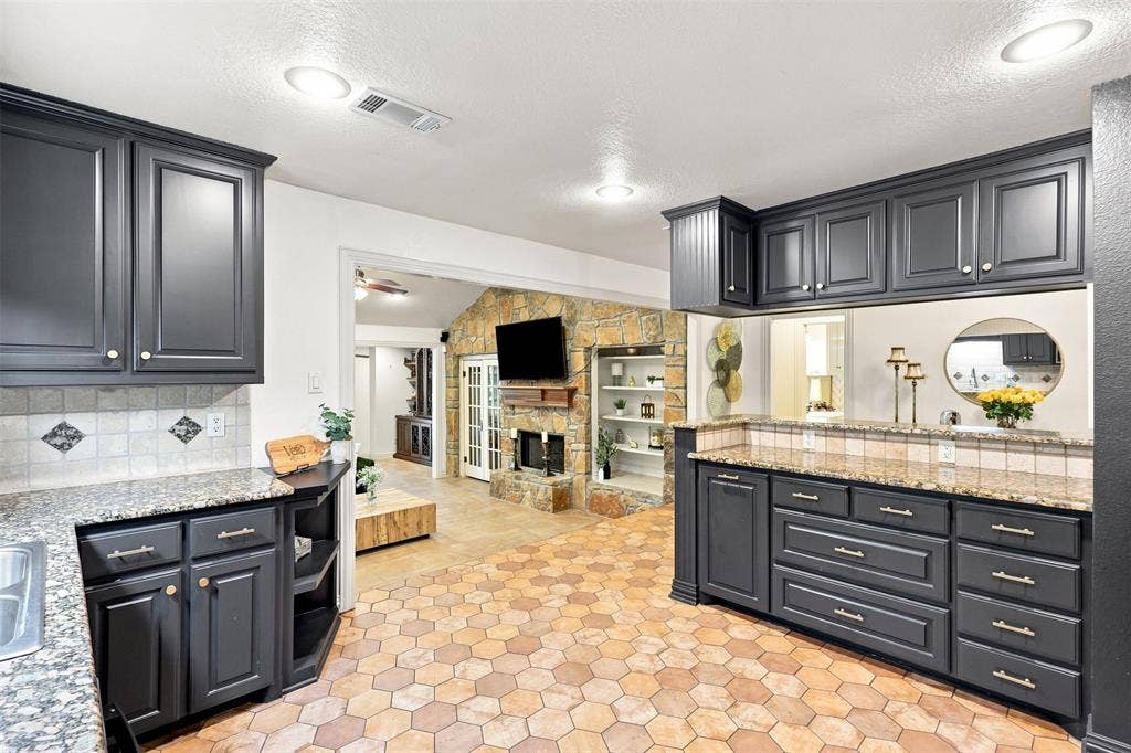 284 Shoreline Drive N, Azle, TX 76020 Dark cabinetry, granite-finish countertops, tile backsplash, hexagonal floor tiles, and a pass-through window