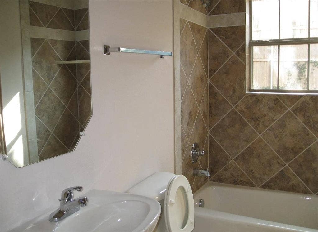 2514 Apollo Villa Road, Garland, TX 75044 Bathroom featuring a ceramic tile shower surround, bathtub with shower fixture, wall-mounted sink, and an octagonal mirror