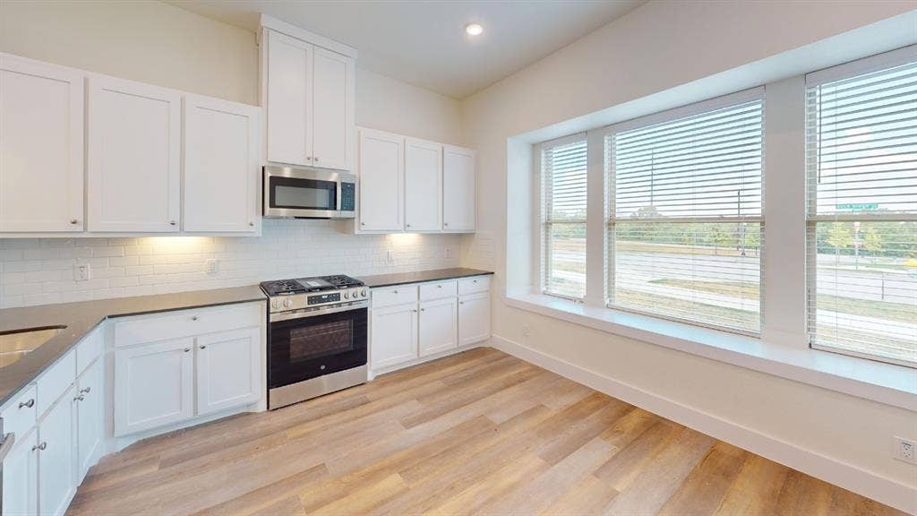 373 Buck Ridge Drive, Frisco, TX 75068 White shaker cabinetry, stainless steel appliances, subway tile backsplash, dark countertops, and wood-finish flooring