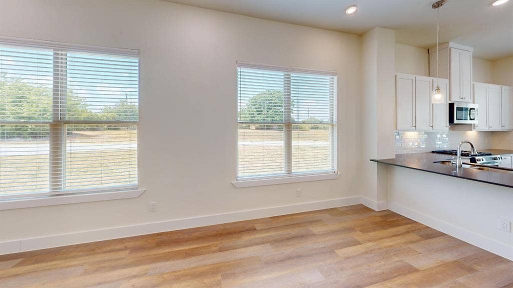 373 Buck Ridge Drive, Frisco, TX 75068 Wood-finish flooring throughout, bright recessed lighting, white cabinetry with under-cabinet lighting, stainless steel appliances, and dark stone countertops