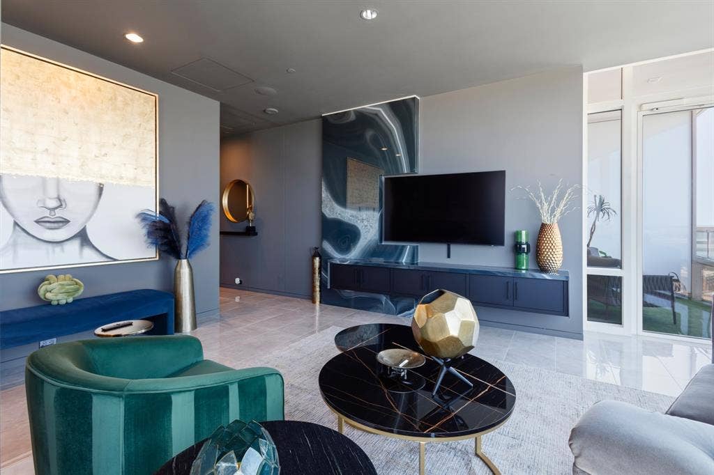 Recessed ceiling lighting, large format tile flooring, a built-in media console, and a wall of windows provide natural illumination