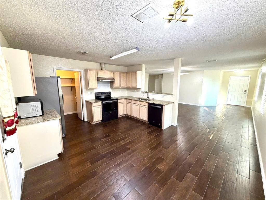 Kitchen featuring wood-finish tile flooring, light-toned cabinetry, granite-finish countertops, and a full suite of black appliances